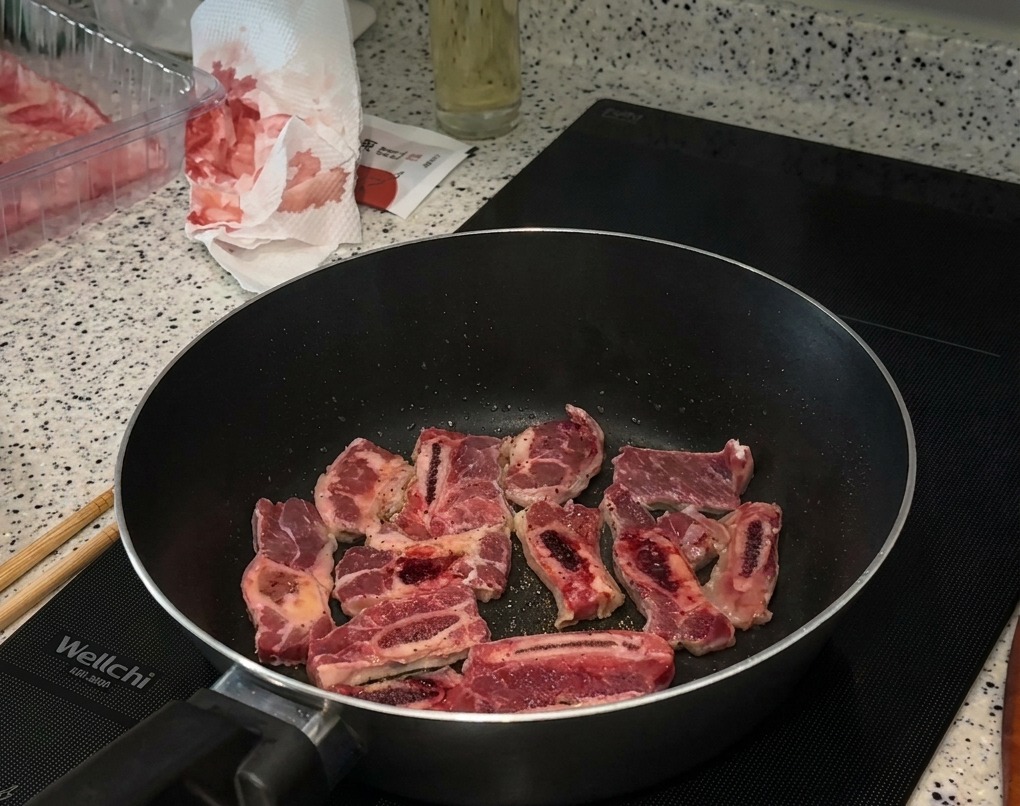 フライパンで焼いている牛肉に、塩とたっぷりの黒胡椒を振りかけている様子。