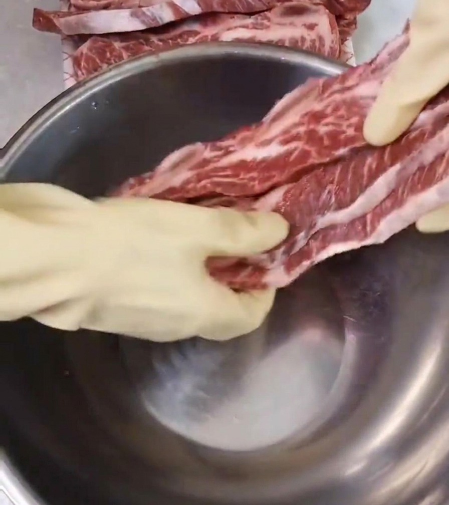 大きなステンレスボウルに、サシの入った生の牛骨付きカルビを入れる様子。