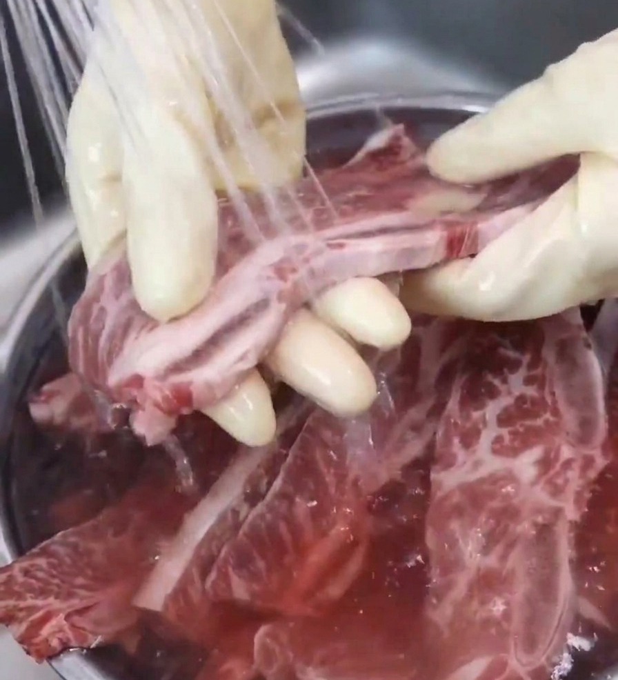 蛇口から流れる冷水で、骨付きカルビを一枚ずつ洗う様子。