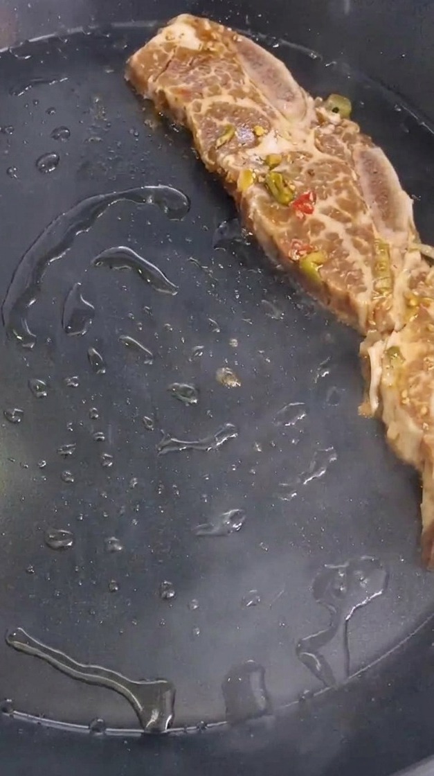 熱したフライパンに、タレに漬け込んだ骨付きカルビを並べて焼く様子。