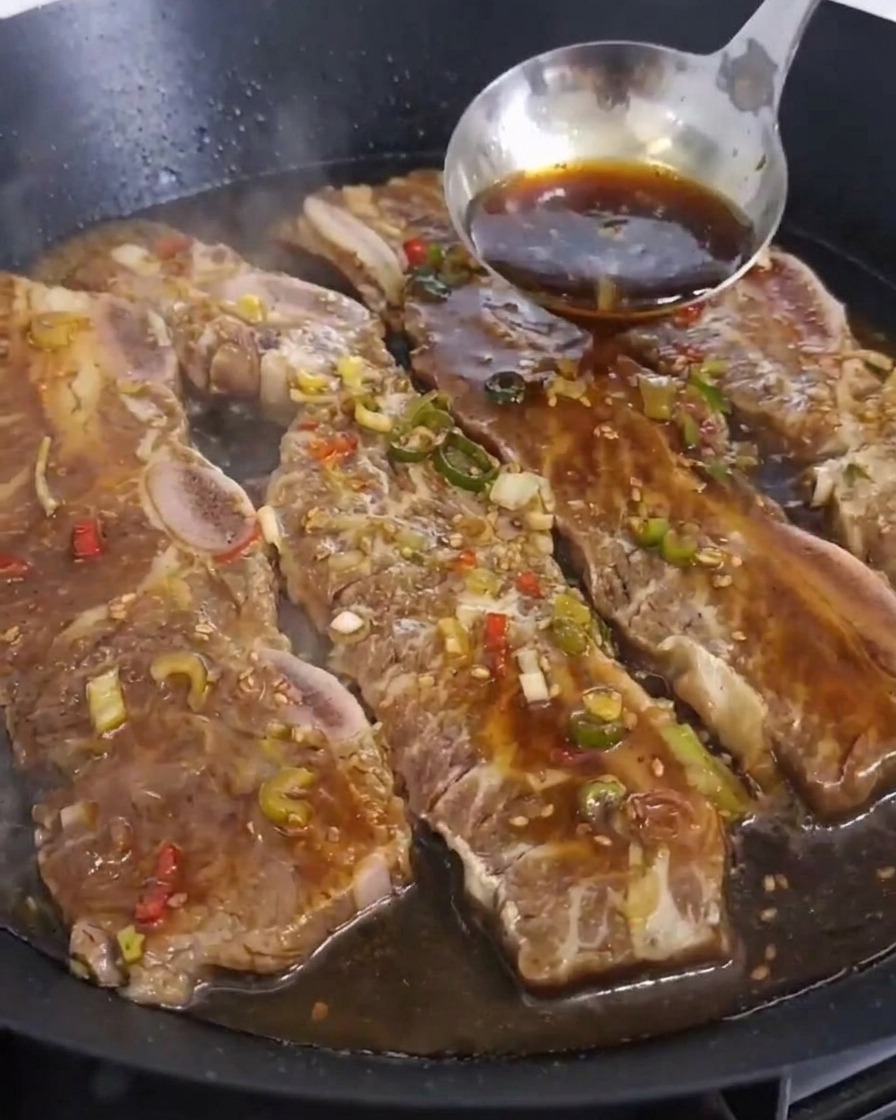 焼いている肉の上から、お玉で濃い茶色のタレをたっぷり注ぐ様子。