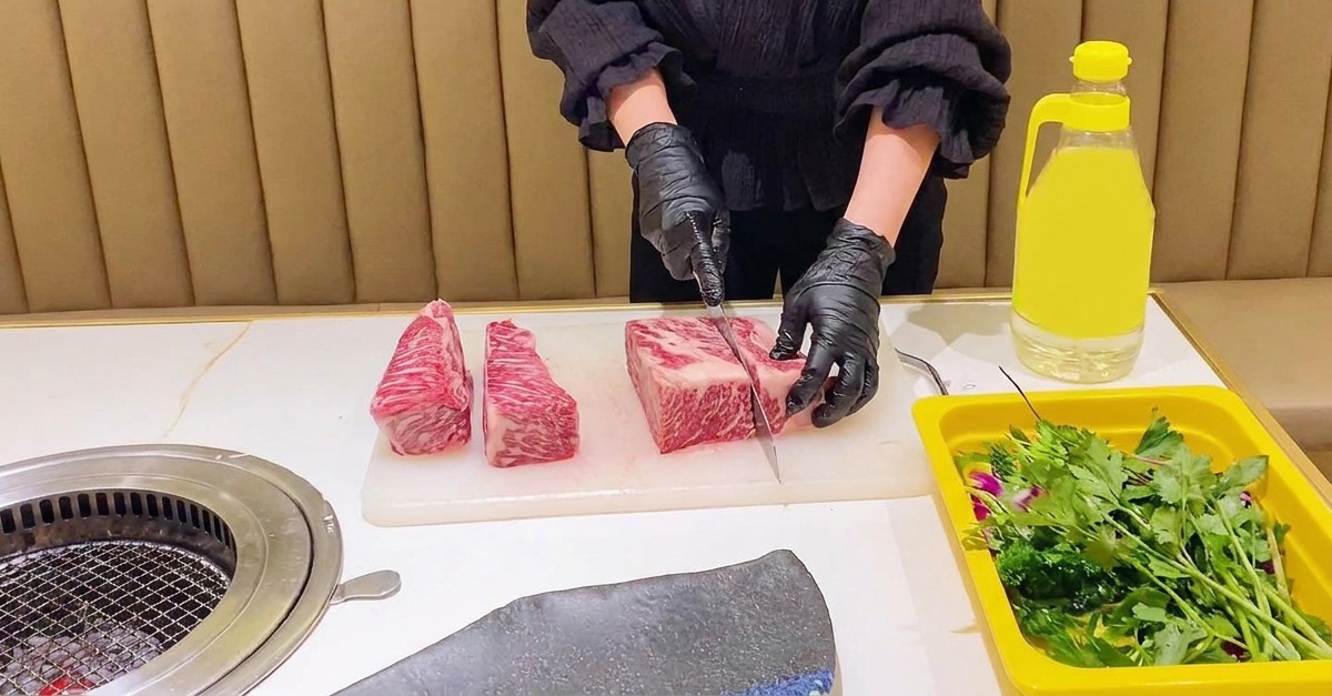 黒い手袋をはめた料理人が、白いまな板の上で大きな霜降り牛ショートリブを均一な長方形に切り分けている様子。