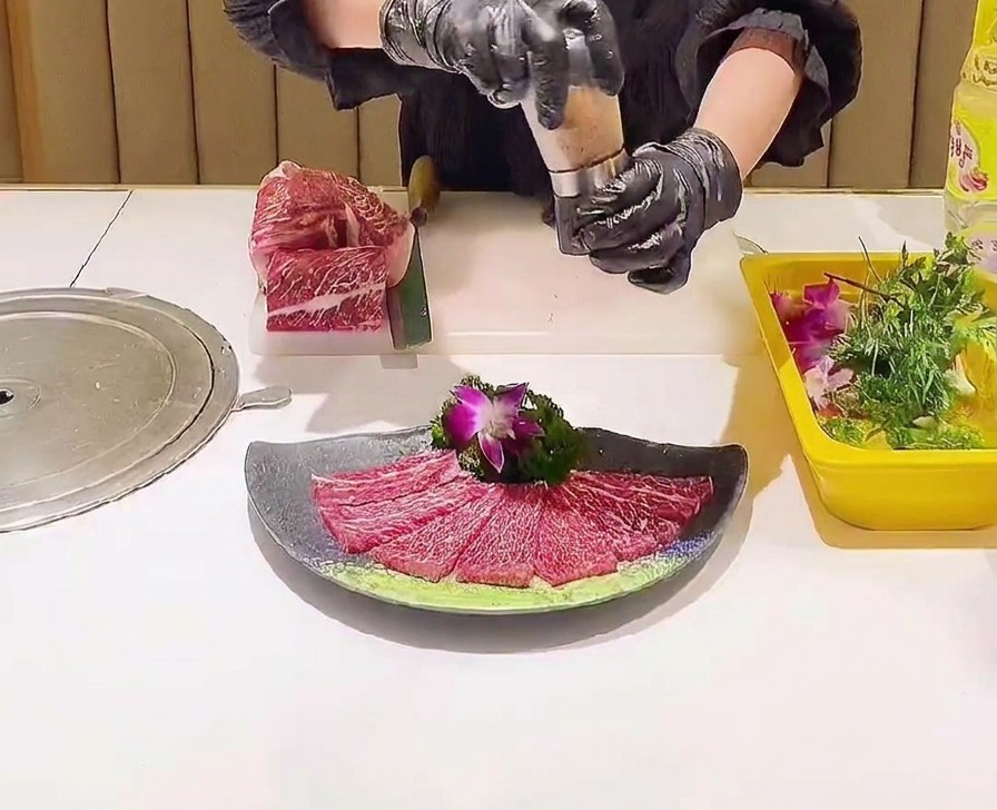 美しく並べられた生の霜降り肉の上に、ミルでピンクソルトを振りかけている様子。