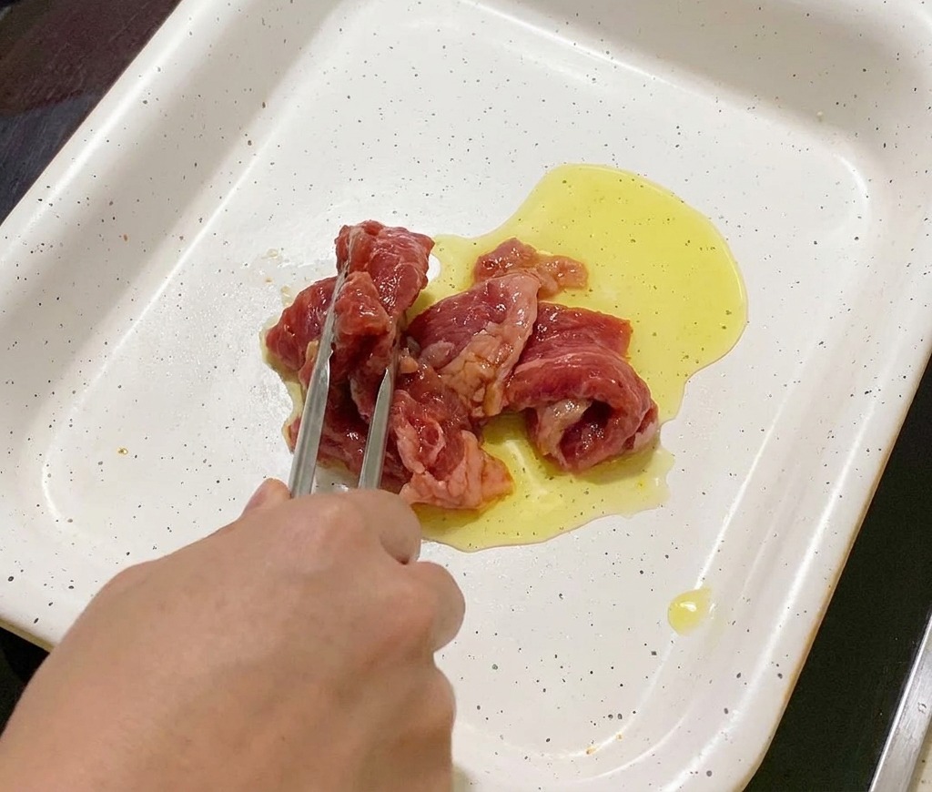 油をひいた白いフライパンに、トングを使って下味をつけた豚肉を広げながら入れている様子。