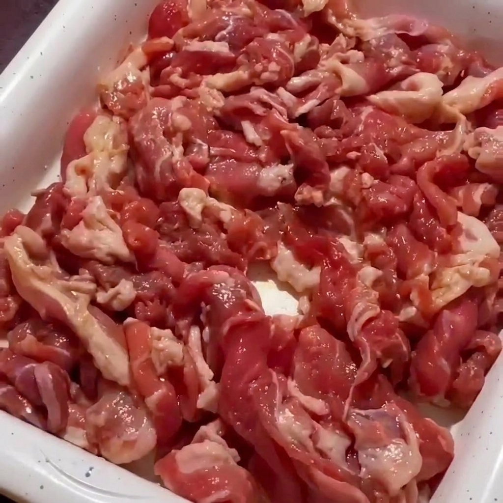 フライパンの中で豚肉が炒められ、縁に焼き色がついて火が通り始めている様子。