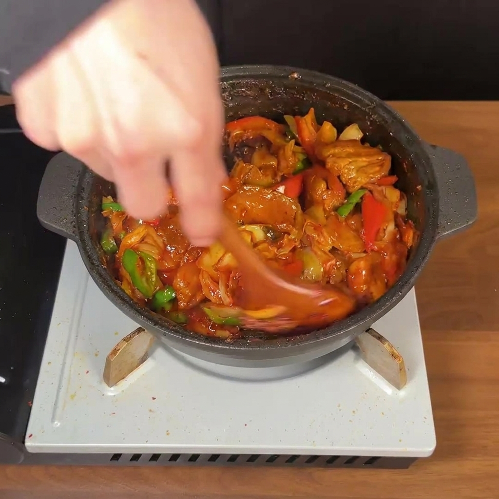木製のスプーンで、濃厚な赤いタレに絡まった肉と野菜を勢いよく混ぜている様子。
