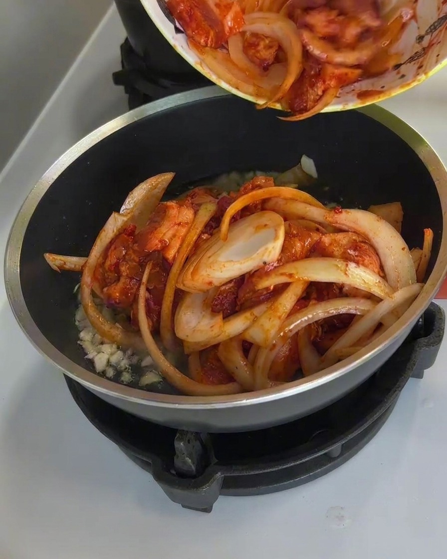 フライパンで豚肉と玉ねぎを炒め、タレが煮詰まって美味しそうな色になっている様子。