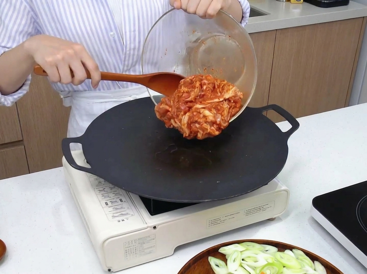 熱した黒いフライパンに、タレに漬け込んだ赤い豚肉を広げて焼いている様子。