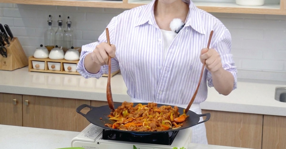 二本の調理ヘラを使って、肉と色鮮やかな野菜を一気に炒め合わせている様子。