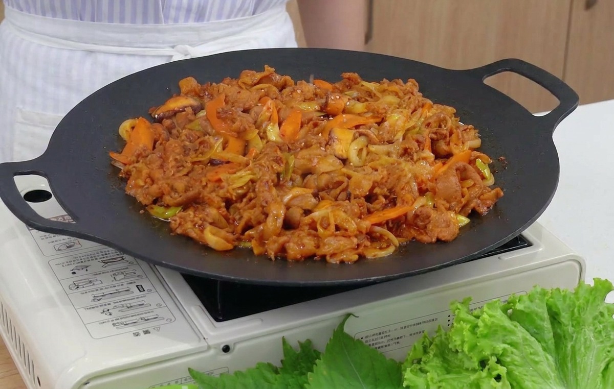 出来上がった熱々の炒め料理の上に、いりごまをパラパラと振りかけているクローズアップ。