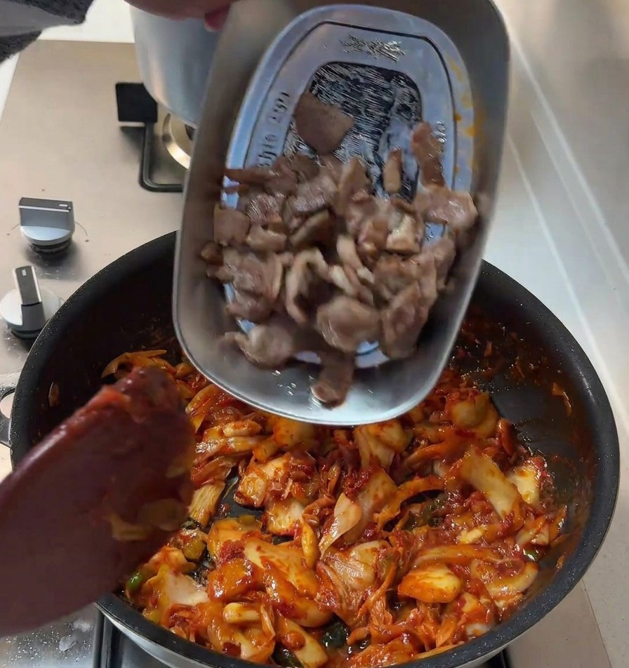 赤いタレで炒めた野菜の中に、先ほど焼いた豚肉を戻している様子。