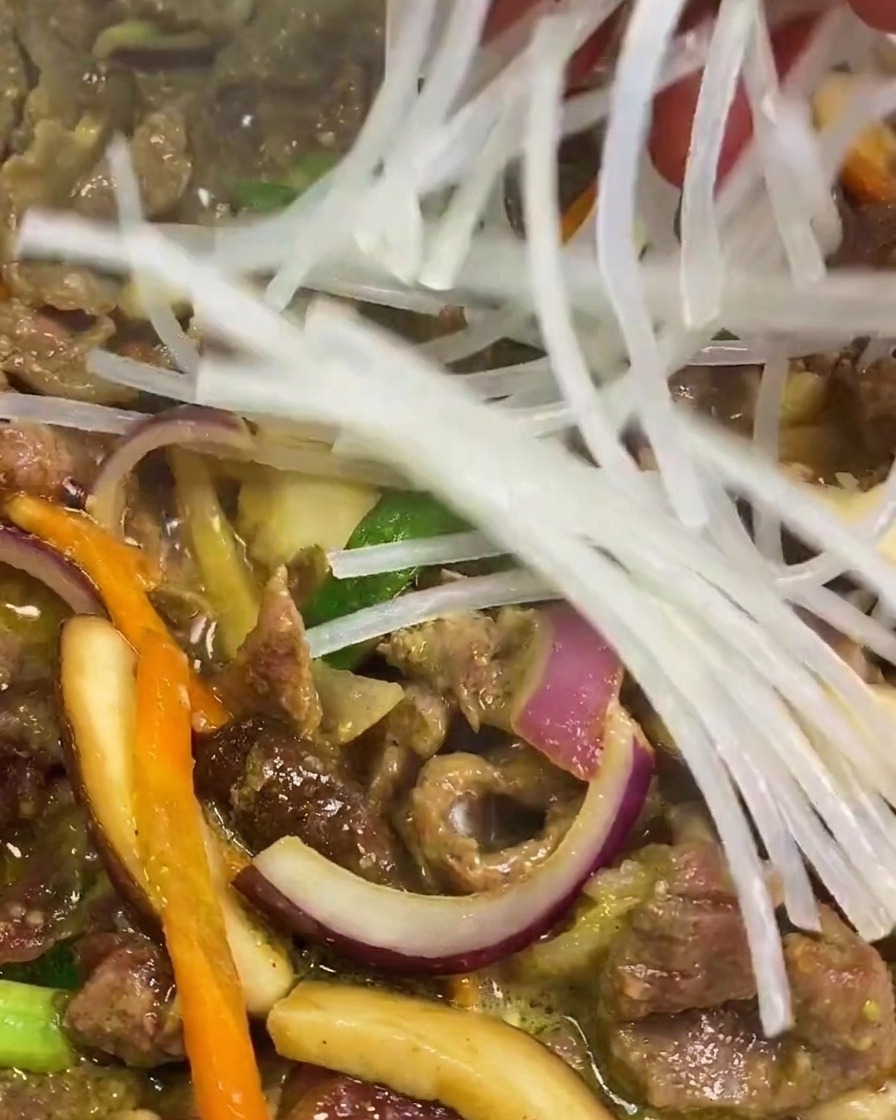 フライパンの牛肉と野菜の上に、水で戻した透明な「さつまいも春雨」をのせている様子。