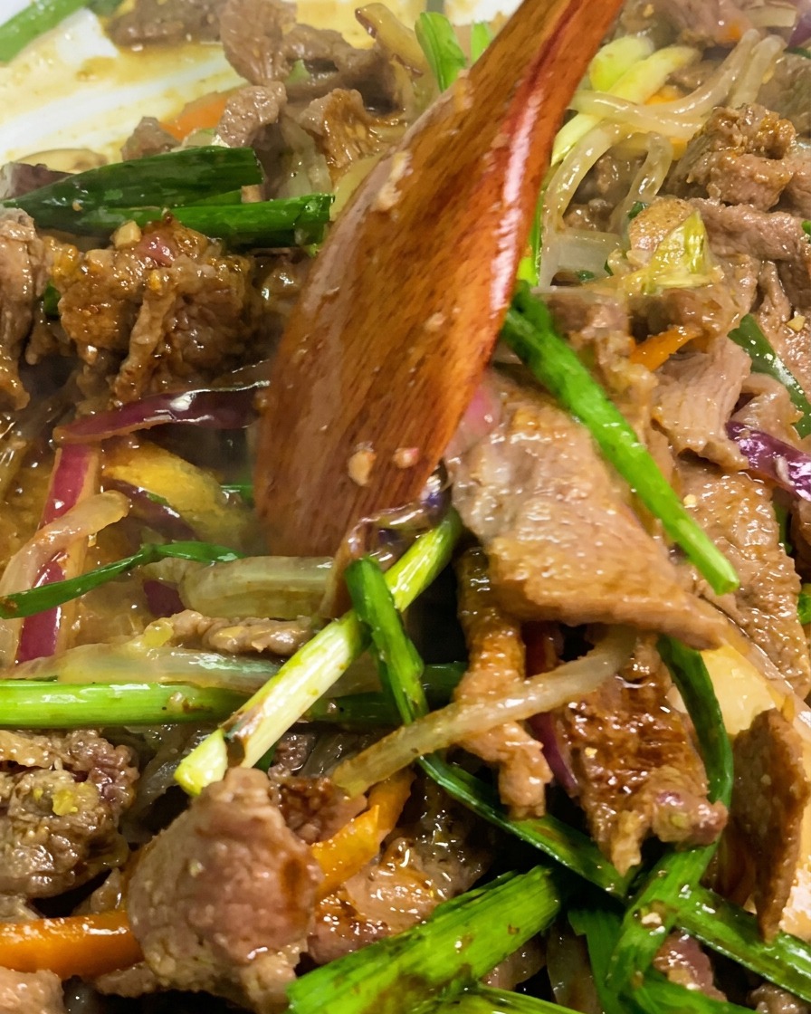 フライパンの中で牛肉、春雨、ニラを木べらで混ぜ合わせ、仕上げをしている様子。