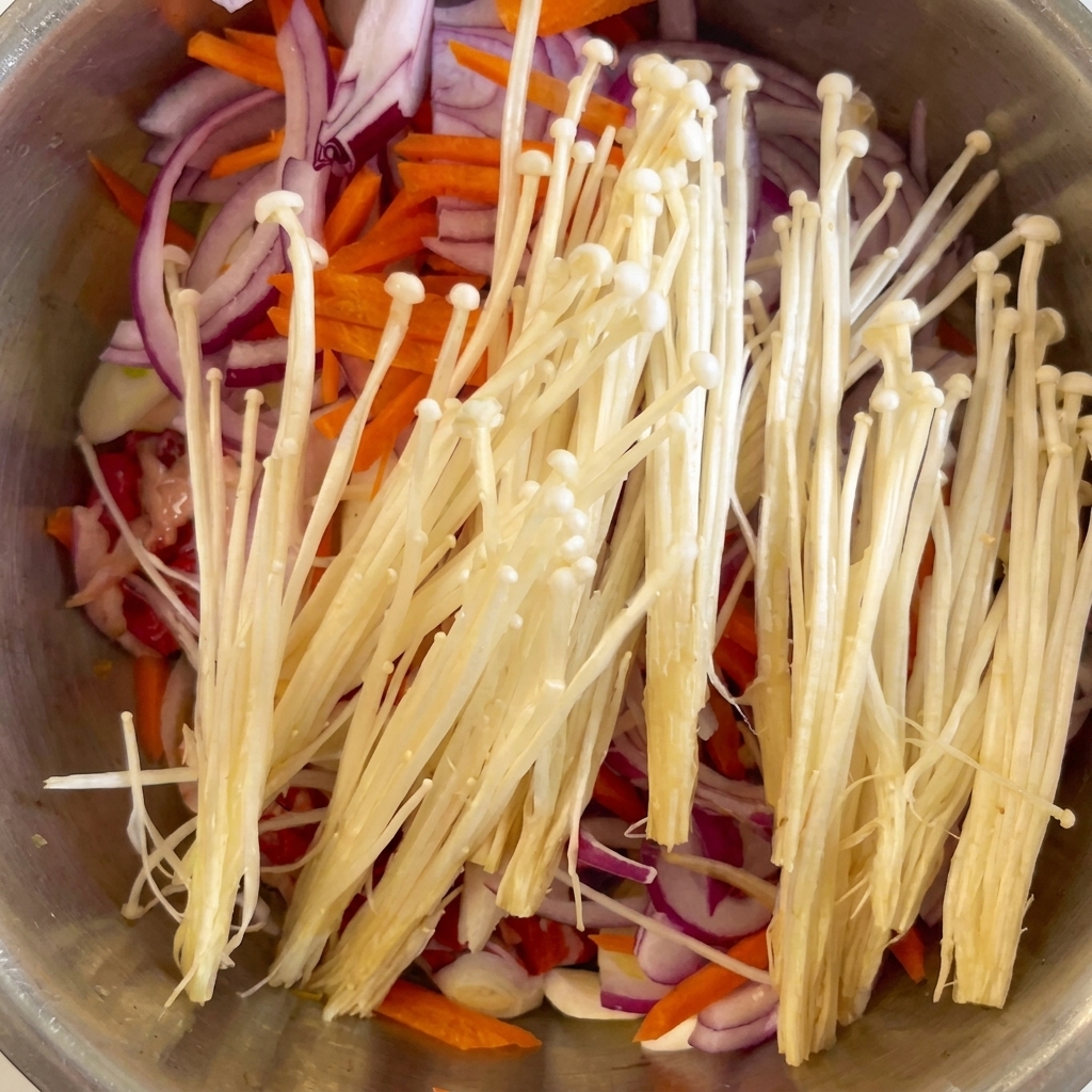 牛肉と野菜の上に、白いえのき茸とおろしにんにくが添えられている様子。