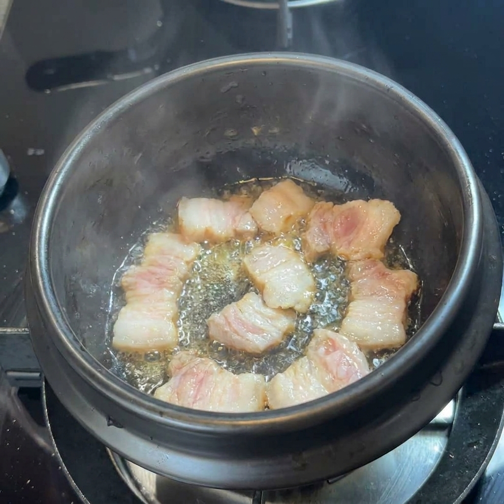 黒い石鍋の底で、自身の脂でジュージューと焼ける豚バラ肉のスライス。