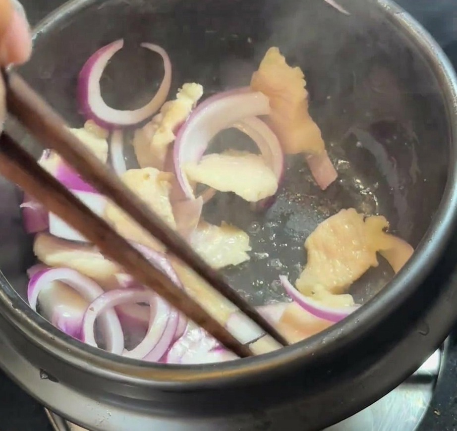 鍋の中で豚バラ肉と溶け出した脂に、スライスした赤玉ねぎを混ぜ合わせている様子。