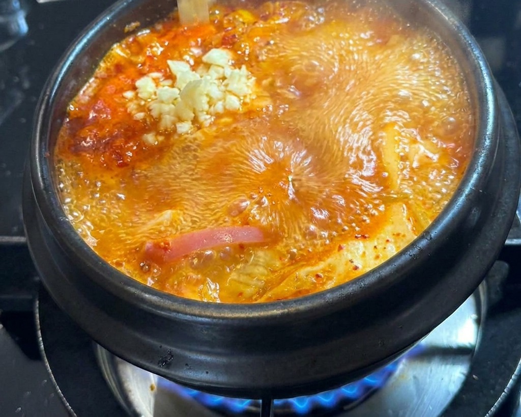 沸騰している赤いスープの中央に、新鮮なおろしにんにくを落としている様子。