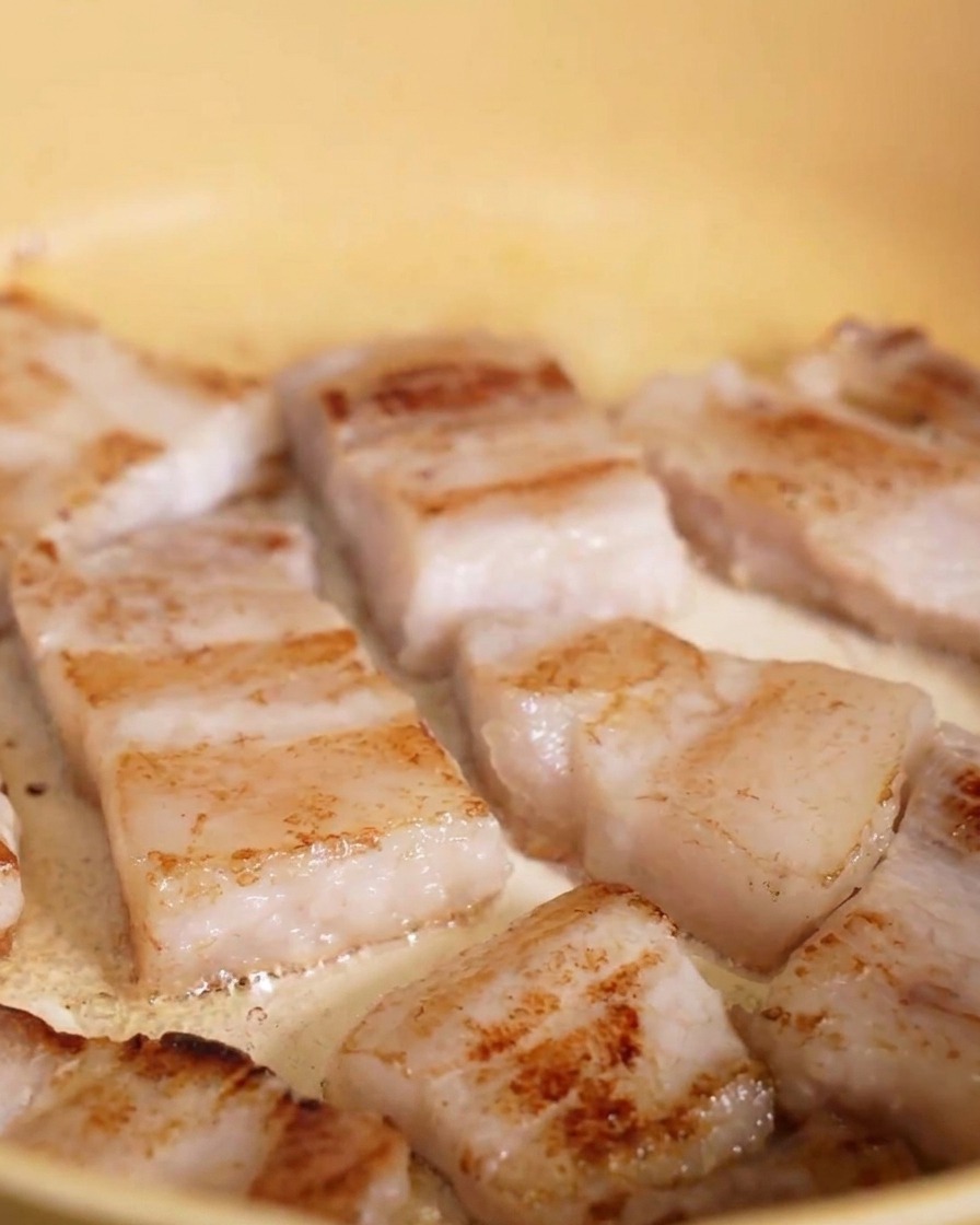 黄色いフライパンで表面がこんがりと黄金色に焼けた豚バラ肉のスライス。