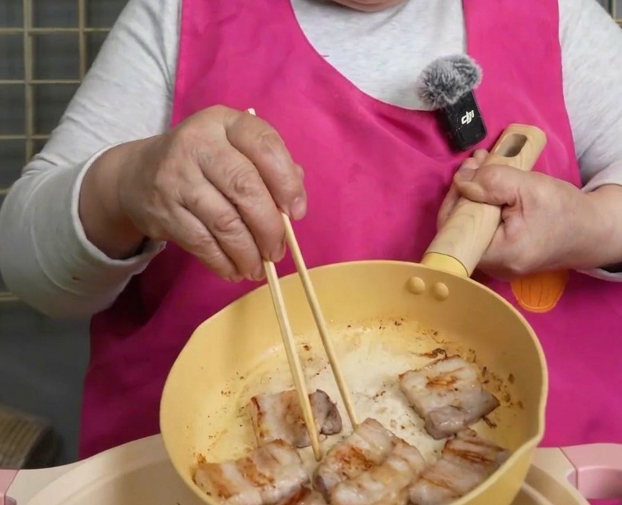 箸を使ってフライパンから鍋へカリカリに焼けた豚バラ肉を移す様子。