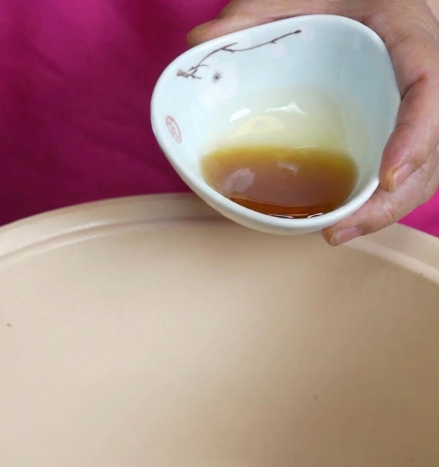 花柄の陶器から琥珀色の香ばしいごま油を鍋に注いでいる様子。