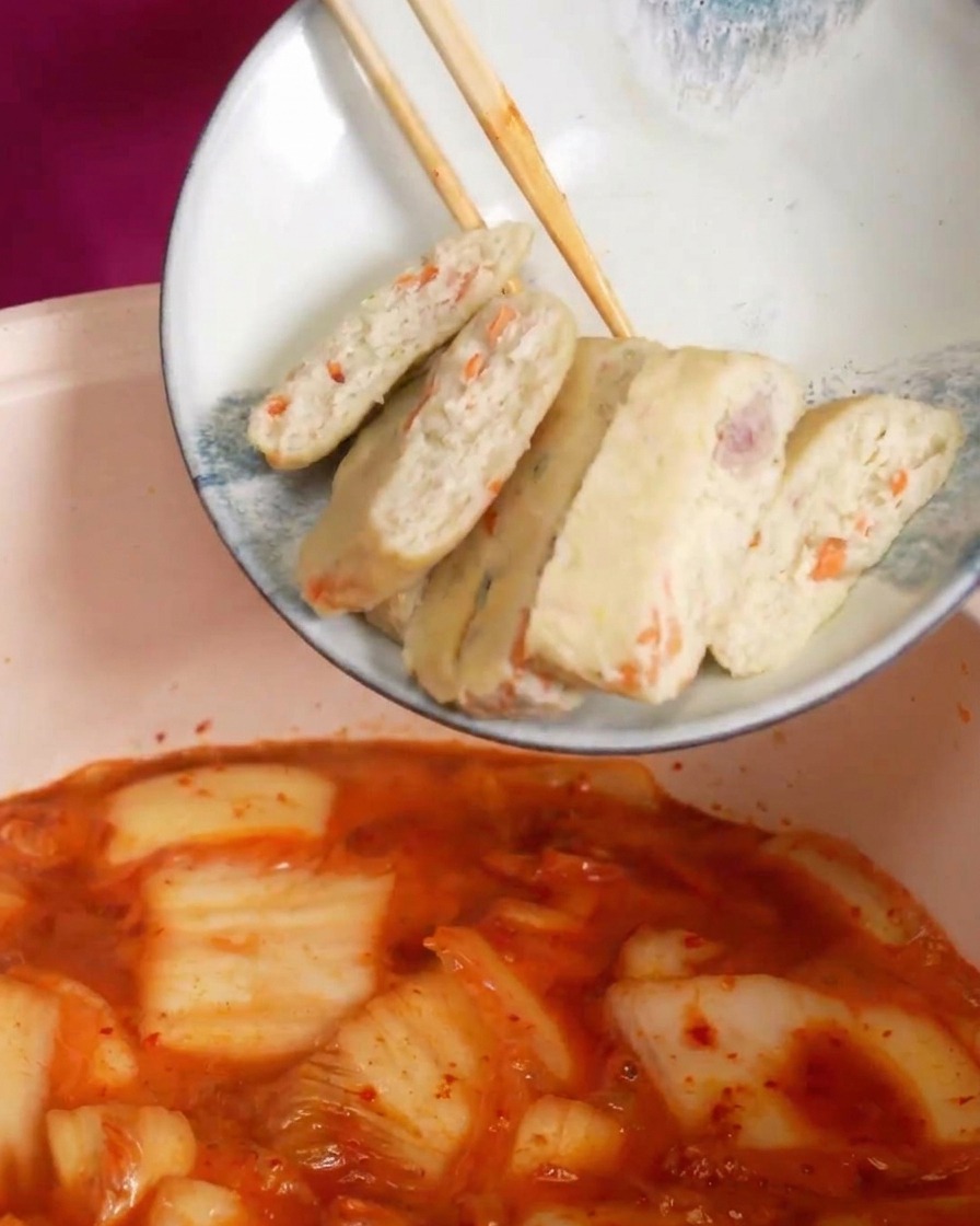 グツグツと沸騰する赤いスープの中にスライスしたさつま揚げを入れる様子。