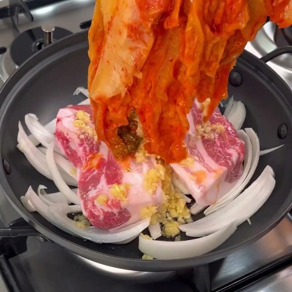 豚バラ肉の上に大きなムグンジ（熟成キムチ）を広げてのせている様子。