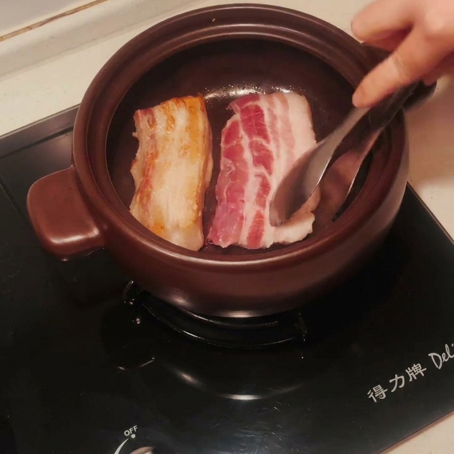 土鍋の中で豚バラ肉をトングで裏返し、片面がこんがりと黄金色に焼けている様子。