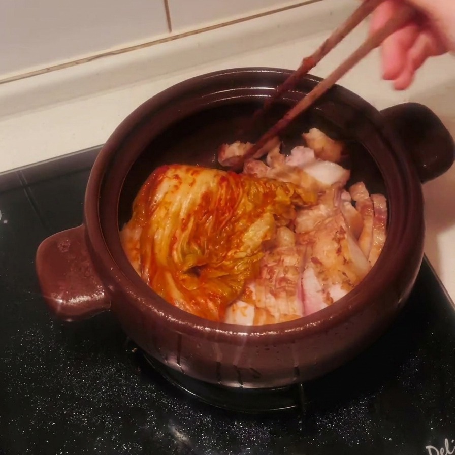 豚バラ肉の上に箸でたっぷりの熟成キムチをのせている様子。