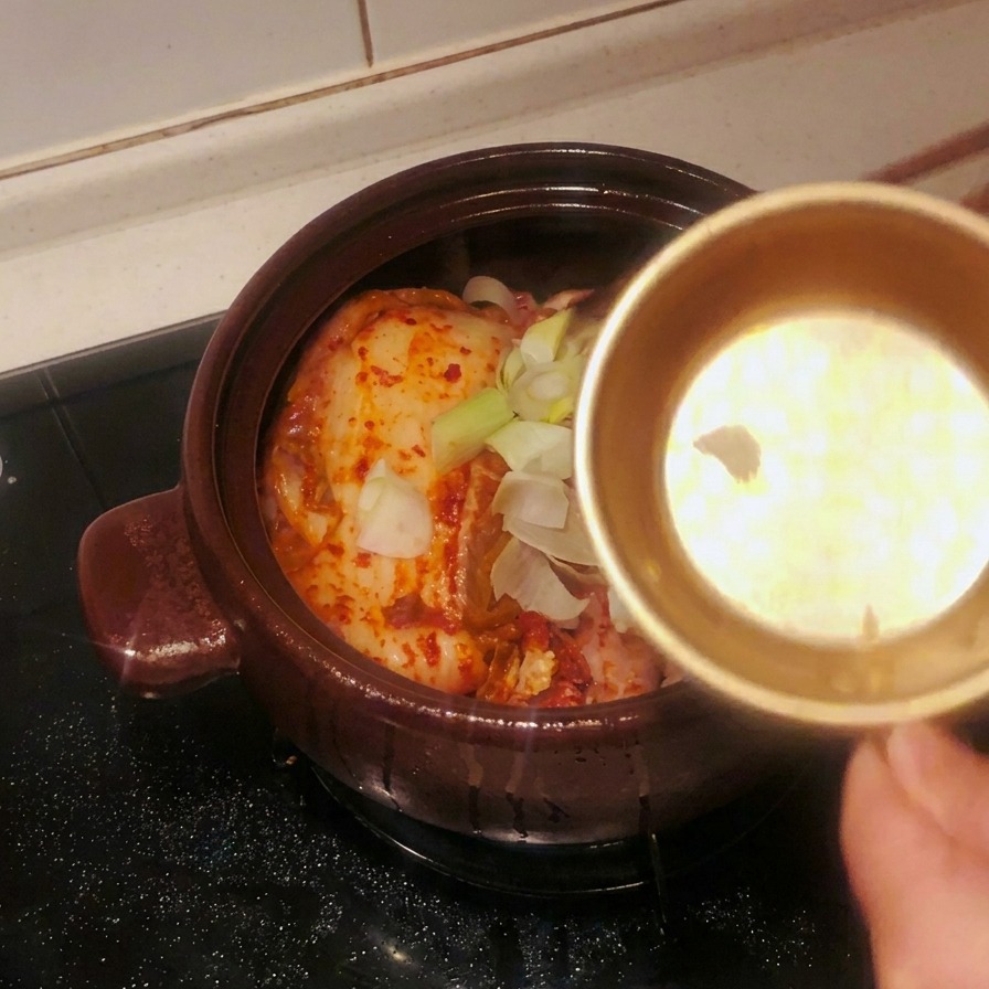 キムチの上にスライスしたニンニクと長ねぎを投入している様子。