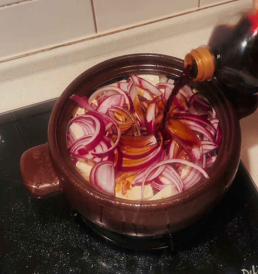赤玉ねぎと豆腐の上に、ボトルから直接醤油を回し入れている様子。