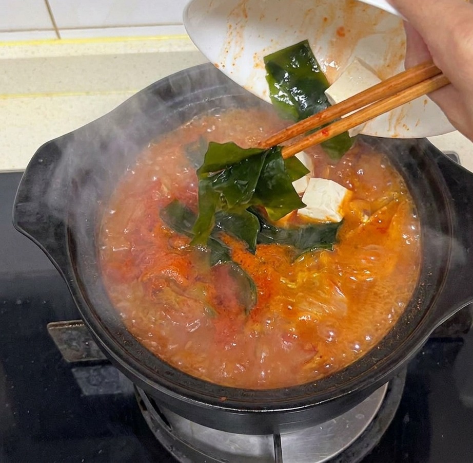 グツグツと煮える赤いスープに、カットした出汁昆布を入れている様子。