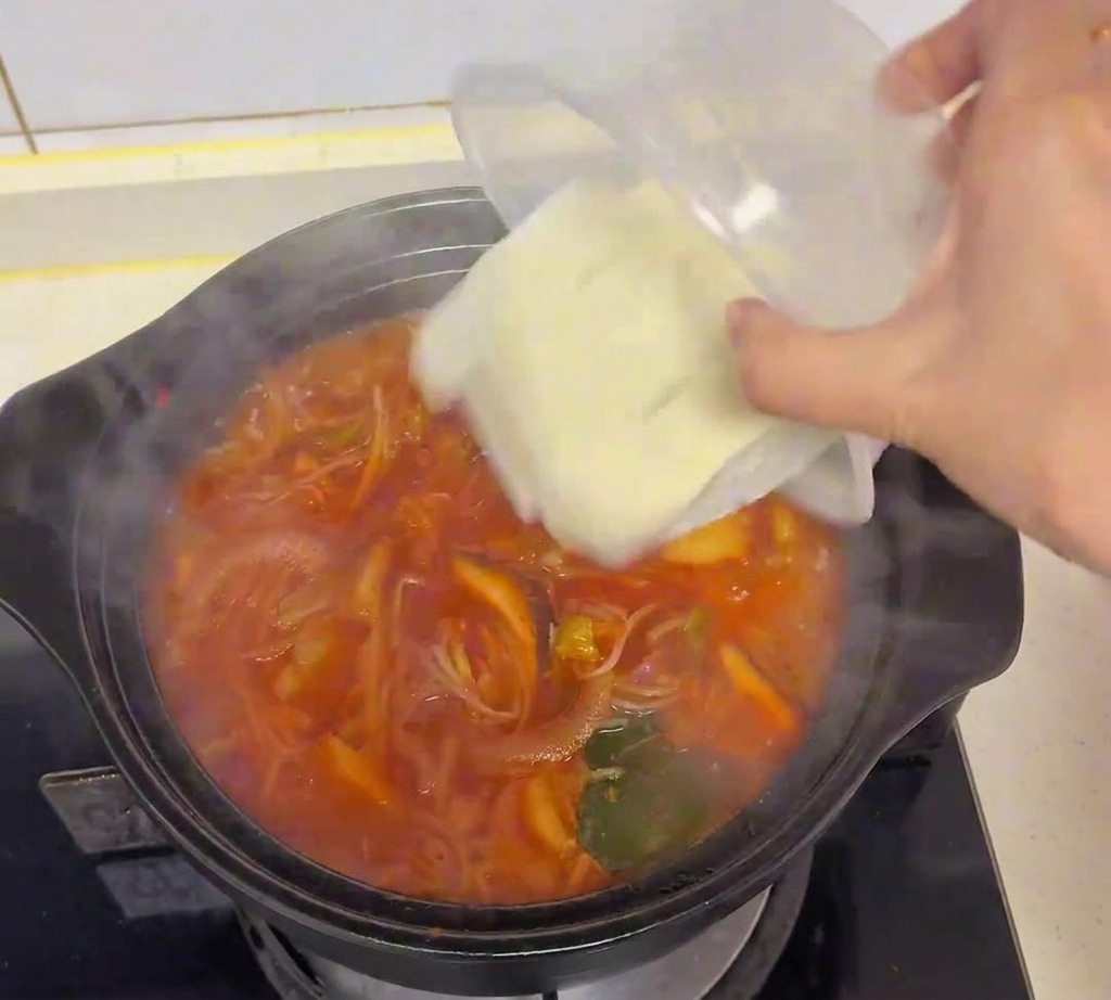 沸騰したスープの中に、白い絹ごし豆腐のキューブを丁寧に入れている様子。