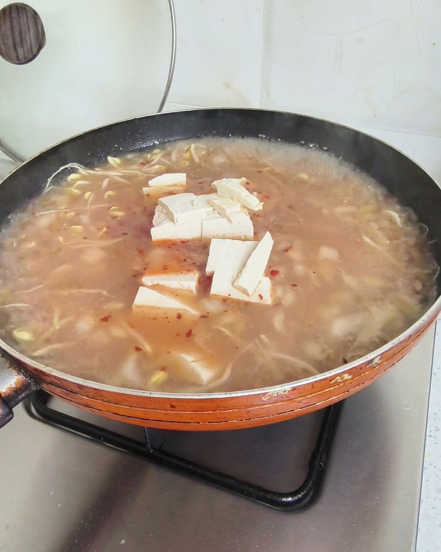 赤みがかったスープの表面に豆腐の角切りを並べている様子