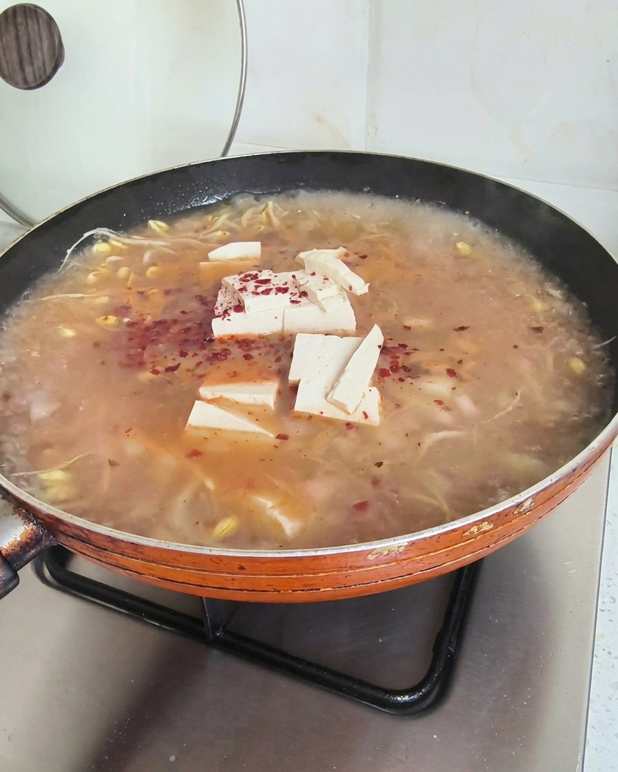 煮込み中のスープの上に赤い粉唐辛子を振りかけている様子