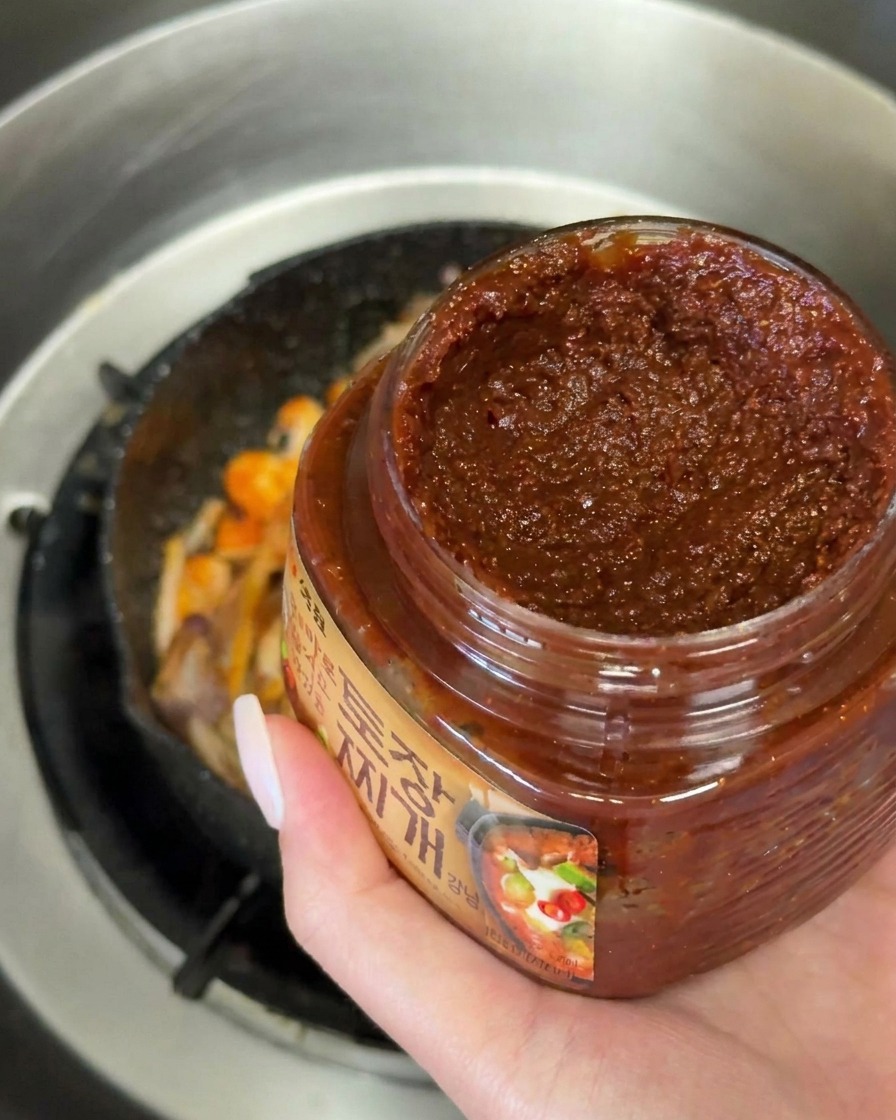 炒めた野菜の上に、スプーン一杯の濃い茶色の韓国味噌を乗せている様子。