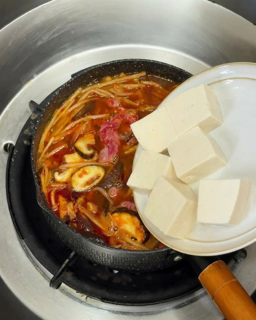 煮え立つスープの中に、カットされた絹ごし豆腐を静かに入れている様子。