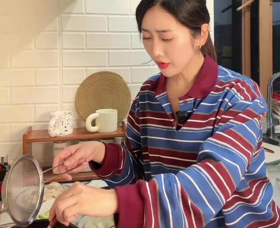 沸騰した鍋に、ザルと金属製のスプーンを使って茶色の韓国味噌を溶かし入れている様子