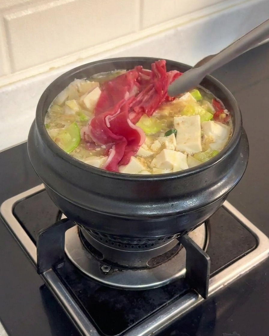 トングを使って、豆腐や野菜が入った沸騰中のスープに薄切りの生肉を入れている様子