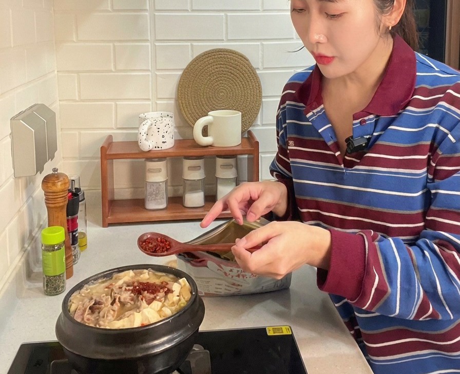 肉や野菜が入ったチゲの鍋に、木のスプーンで鮮やかな赤色の粉唐辛子を振りかけている様子
