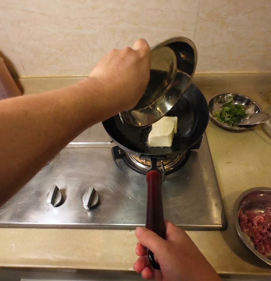 熱した油の入った中華鍋に、白い木綿豆腐を丸ごと1丁入れている様子。