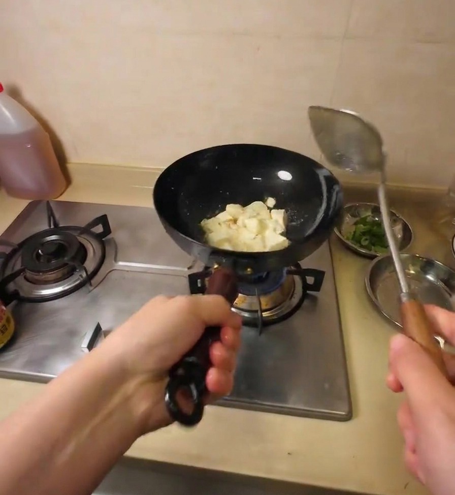 金属製のヘラで豆腐を一口サイズに崩しながら、油で炒めている様子。