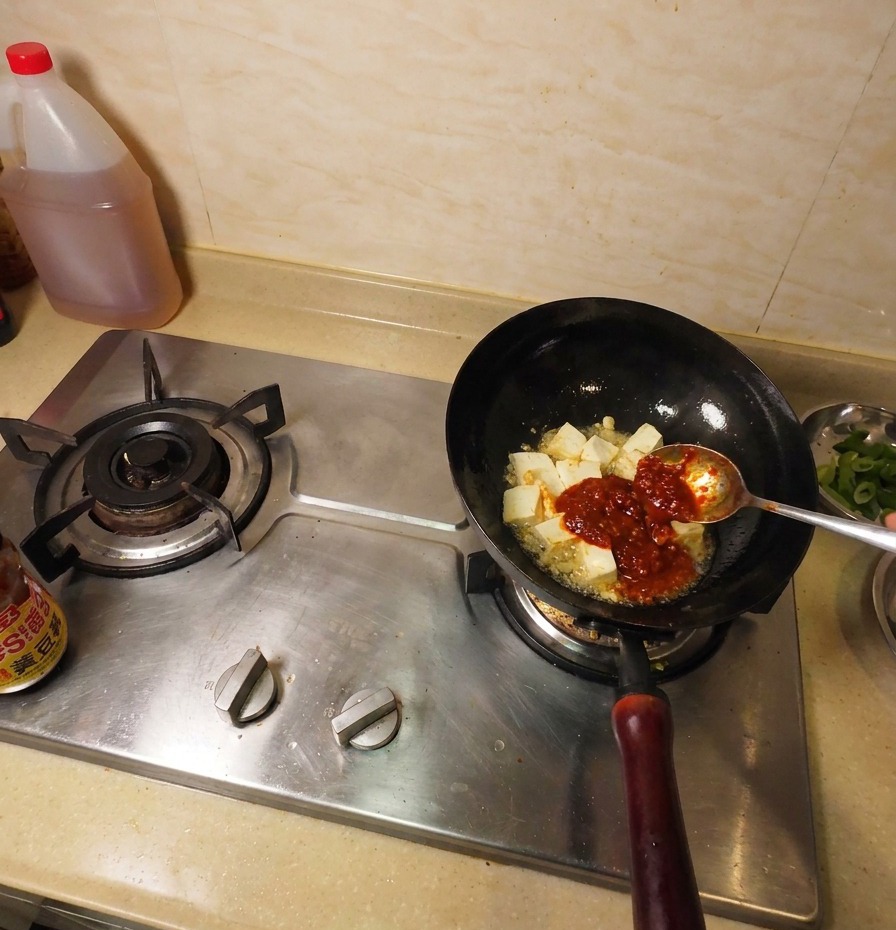 チリソースで和えた豆腐が入った鍋に、韓国味噌(テンジャン)を加えている様子。