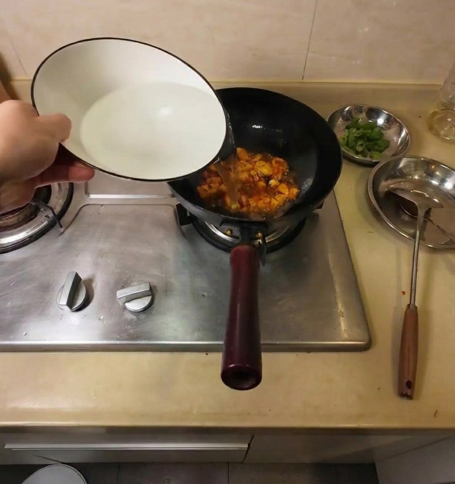 豆腐と調味料が入った中華鍋に、白い器からお湯を注いでいる様子。