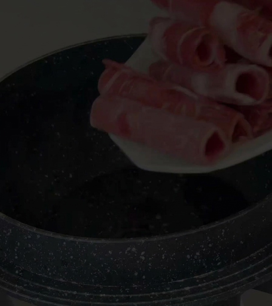 黒い鍋の中に、薄切りの生の牛肉を入れている様子