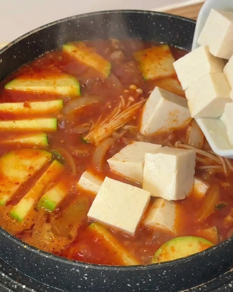 スープが煮立つ鍋に、角切りにした白い豆腐を加えている様子