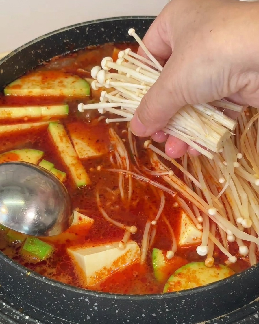 豆腐やズッキーニが入った鍋に、えのきだけを加えている様子