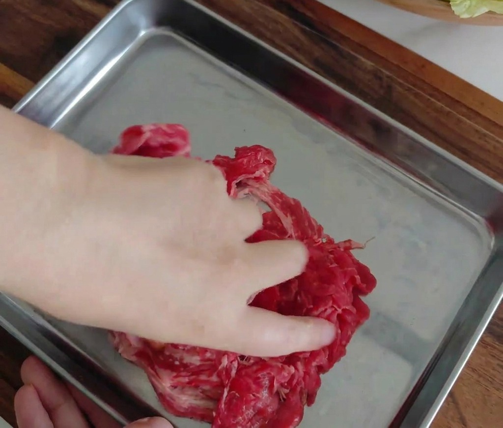 金属製のバットの中で、牛肉にスパイスを手で揉み込んでいる様子。