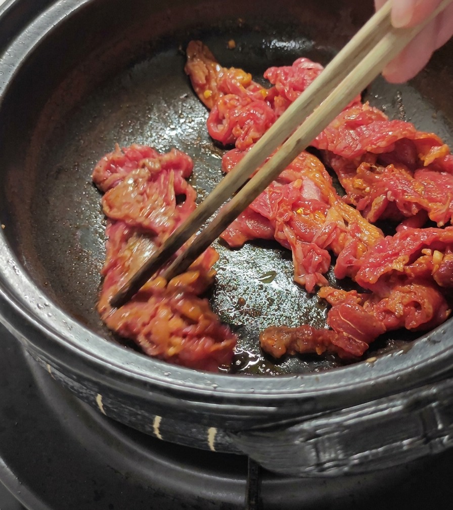 黒い鍋の中で、味付けした牛肉を菜箸で炒めている様子。