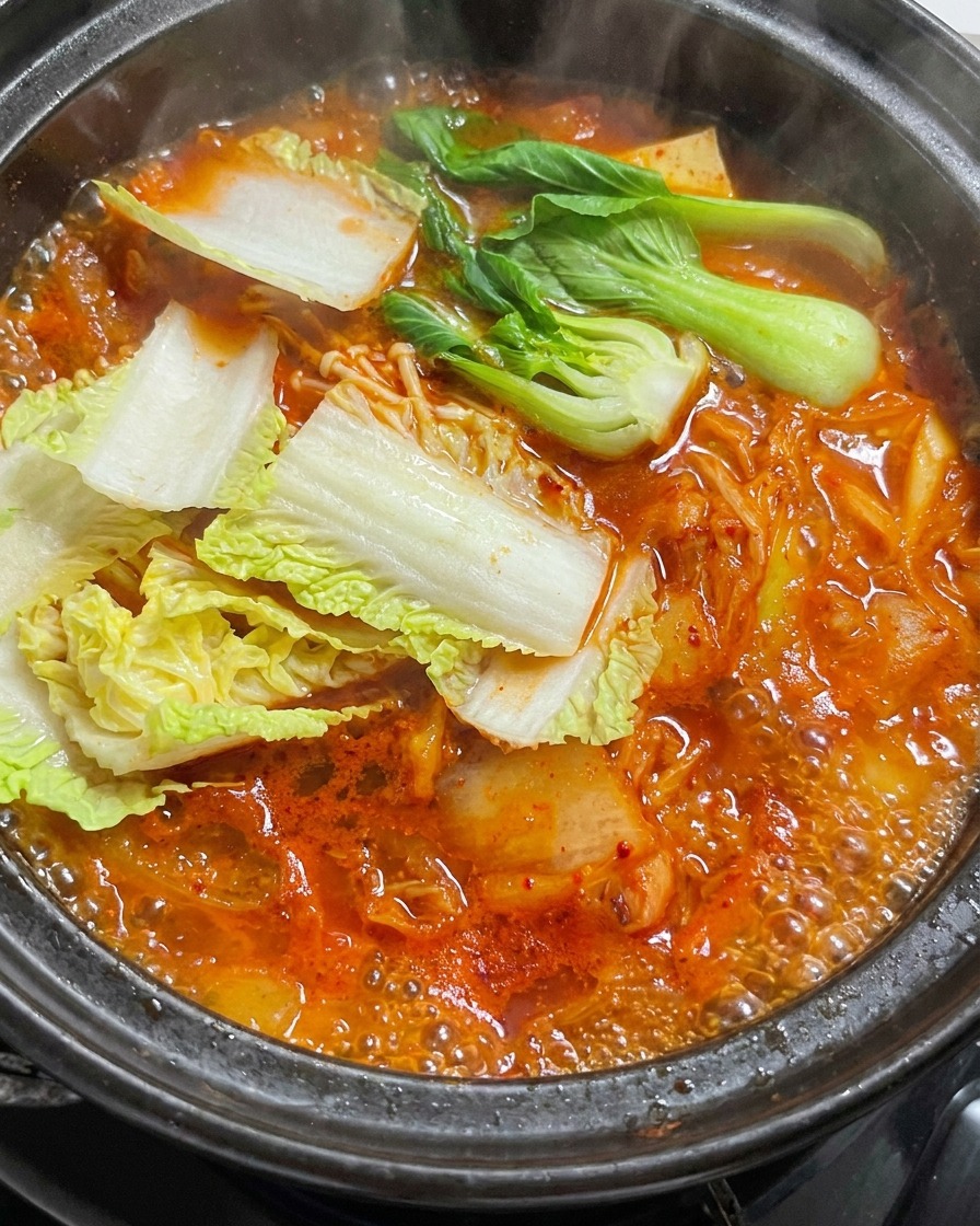 ぐつぐつ煮立つ赤いスープが入った石鍋に、新鮮な白菜の葉を入れている様子。
