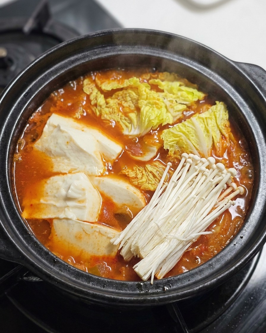 煮立つ赤いスープの上に、牛肉、えのき茸、青ねぎをのせている様子。